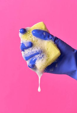 Eldivenli elini sarı hijyenik sünger sıkıştırma. Su, köpük. Pembe bir arka plan.