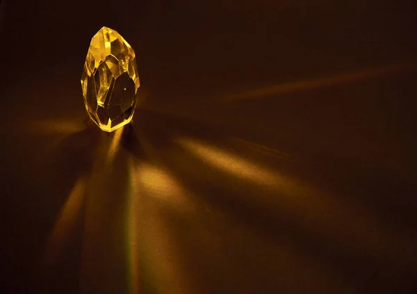 Rays of light passing through a large yellow quartz crystal on a dark brown background.