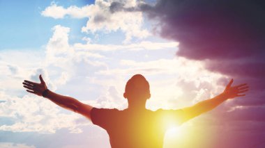 Gün batımında kollarını açmış genç bir adam.