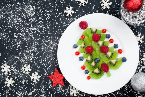 Kiwi christmas tree with raspberry, blueberry and cowberry on table with decoration Stock Picture