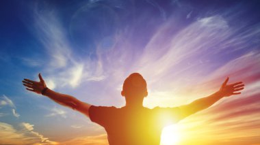 Young man standing outstretched at sunset. Bright solar glow and sky clipart