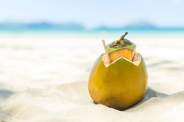 Fresh young coconut lying on the sand beach background with straw ready for drink. — Stock Photo, Image