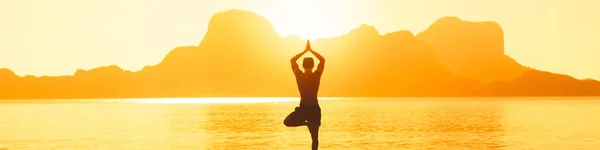 人类站在岩石旁的海滩上, 在海上惊人的日落中练习瑜伽 — 图库照片