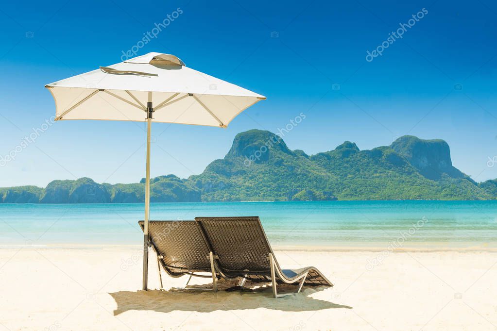 Two beach chairs under a blue umbrella on the white sandy beach