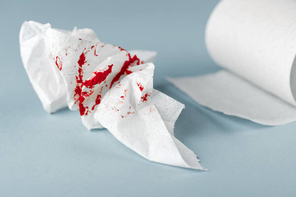 A photo of used bloody toilet paper and a toilet paper roll on the light blue background
