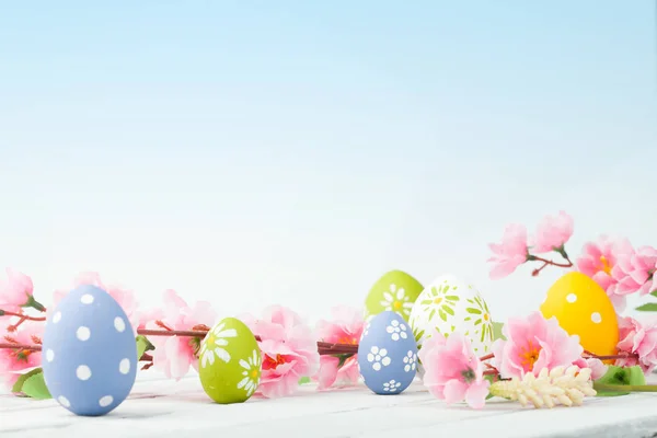 Huevos de colores con flores rosadas sobre fondo de madera blanca — Foto de Stock