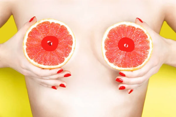 Sexy joven mujer sosteniendo pomelos cerca de sus pechos en el fondo de color. Concepto erótico —  Fotos de Stock