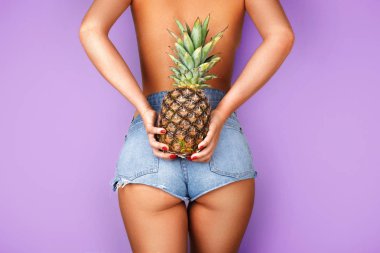 Mor arka planda elinde ananas tutan genç bir kadın. Spor ve sağlık konsepti.