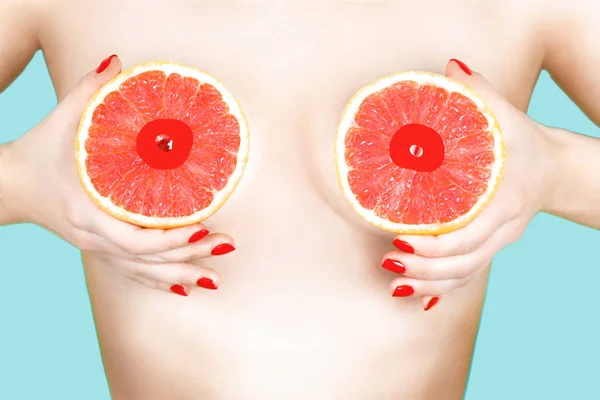 Sexy joven mujer sosteniendo pomelos cerca de sus pechos en el fondo de color . —  Fotos de Stock