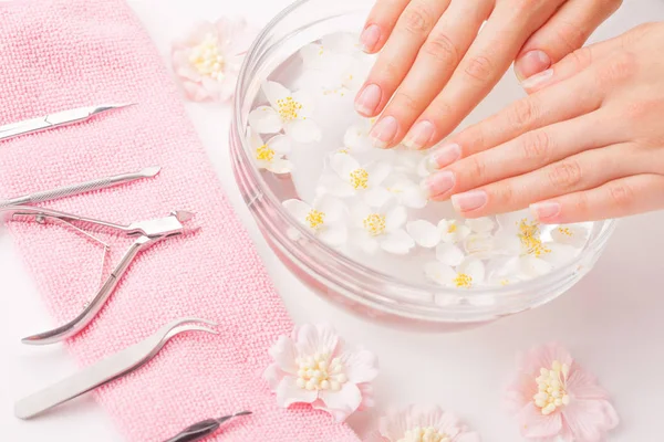 Manos de mujer con uñas de manicura y tazón con agua y flor de margarita . —  Fotos de Stock