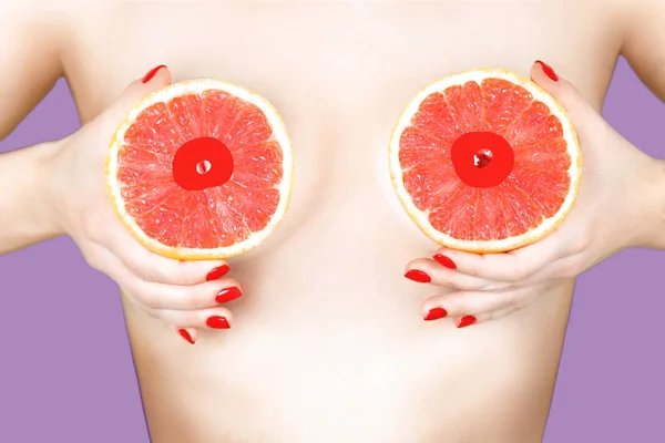 Sexy joven mujer sosteniendo pomelos cerca de sus pechos en el fondo de color . — Foto de Stock