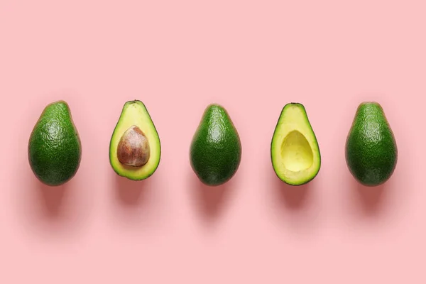 Rij verse gehelen en helften van biologische avocado met kernels in het midden op roze achtergrond. Top View — Stockfoto