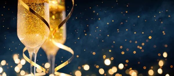 Két pohár pezsgő arany konfettiával, csillogás, szerpentin és világítás. — Stock Fotó