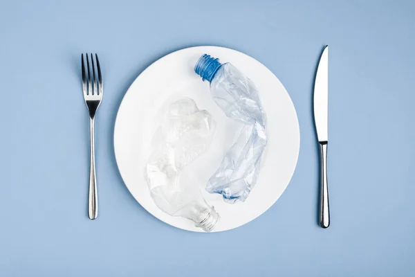 Vista superior de la basura de plástico en la placa blanca, cuchillo y tenedor — Foto de Stock