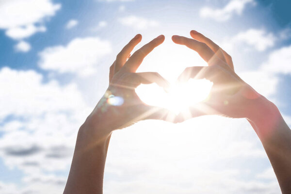 Сердце пальцев против голубого неба и солнца