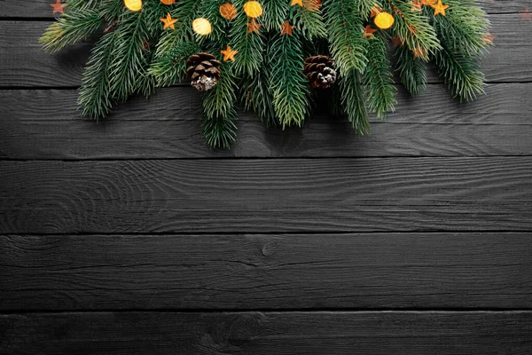 Ramas de árboles de Navidad, conos de abeto y luces doradas sobre fondo de madera negro — Foto de Stock