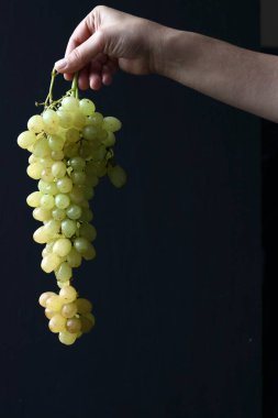 Siyah arka planda bir demet üzüm tutan yeşil üzümler.