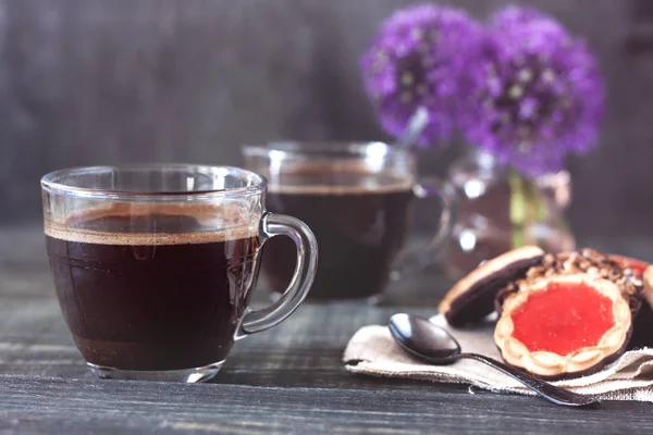 A cup of coffee with delicious biscuits with jam and chocolate icing on a wooden table