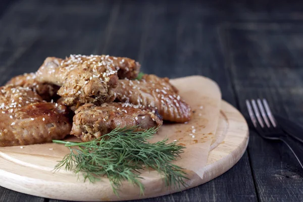 Fried chicken wings on a rustic serving board, on a black wooden background