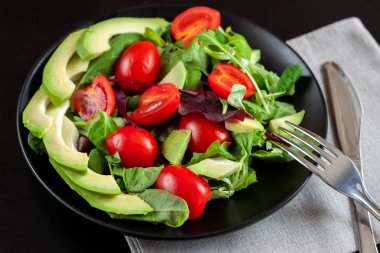 Diyet karanlık bir arka plan üzerinde siyah bir plaka üzerinde avokado salatası.
