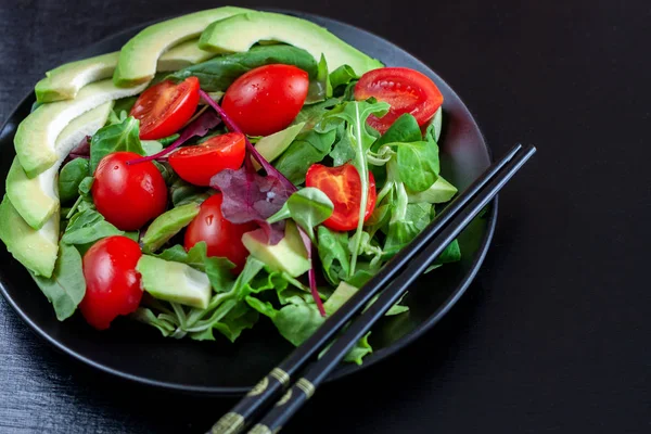 在黑暗背景上的黑色盘子上的配鳄梨的膳食沙拉 — 图库照片