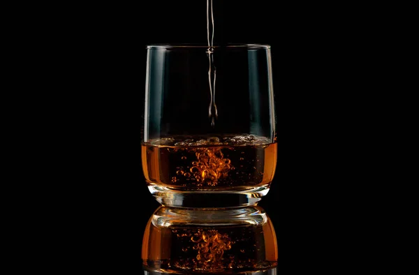 Il brandy viene versato in un bicchiere su uno sfondo nero — Foto Stock