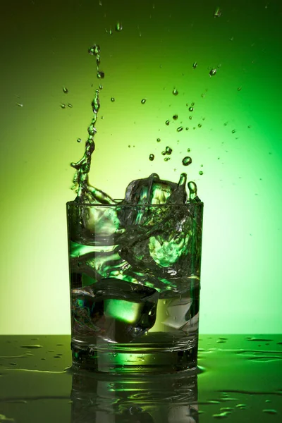 Schizzi in un bicchiere d'acqua su sfondo colorato — Foto Stock