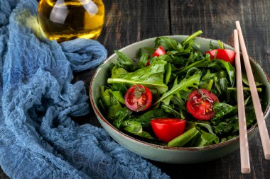 Siyah ahşap masada domates, arugula ve ıspanak salatası