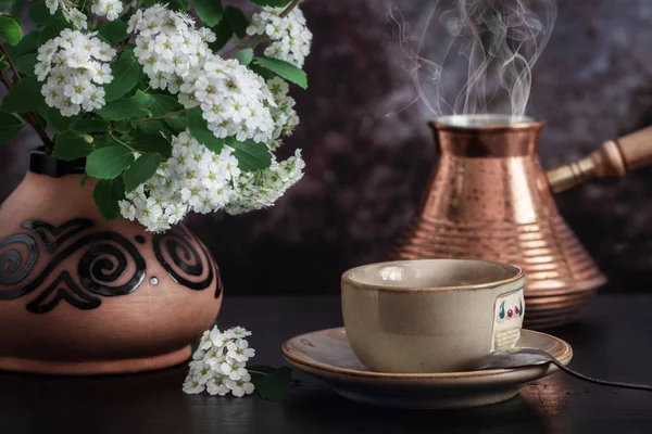 Az asztalon van egy csésze kávé és egy váza, fehér virágai spirea — Stock Fotó