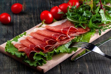 Masada dilimlenmiş Jamon, domates ve otlar ile ahşap bir kesme tahtası