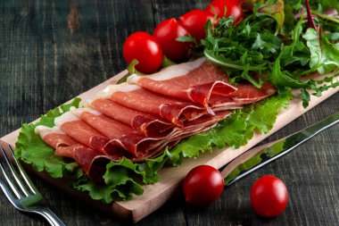 Masada dilimlenmiş Jamon, domates ve otlar ile ahşap bir kesme tahtası