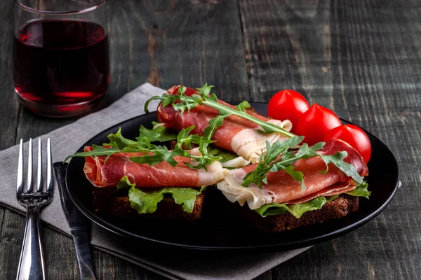 Op de tafel is er een schotel met Jamon sandwiches, tomaat, greens en een glas rode wijn — Stockfoto