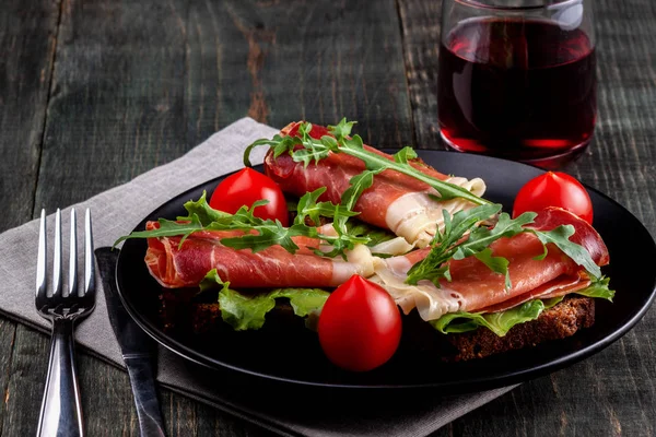 Op de tafel is er een schotel met Jamon sandwiches, tomaat, greens en een glas rode wijn — Stockfoto