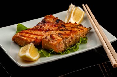 Siyah bir masada bir tabakta limon ile ızgara alabalı