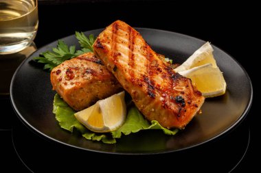 Grilled trout with lemon on a platter on a black table clipart