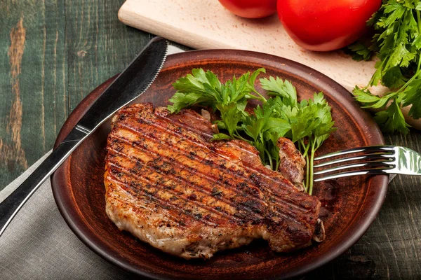 Ein Stück gebratenes Schweinefleisch mit Kräutern auf einer weißen Schüssel auf einem Holztisch, Nahaufnahme — Stockfoto