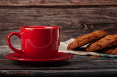 Bir fincan çay, arka planda kurabiyeler, ahşap bir masanın üstünde.