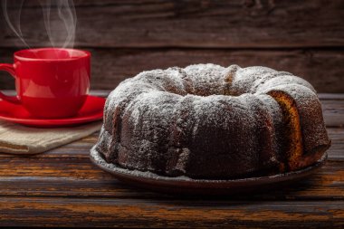 Koyu ahşap bir masada balkabaklı kek ve arka planda çay olan bir fincan.