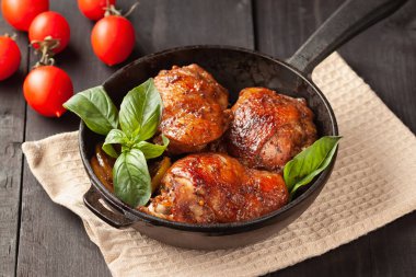 Tahta bir masada, tavuk butları ve fesleğen siyah dökme demir bir tavada