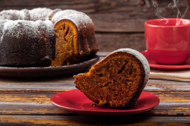 Koyu renk ahşap bir masada balkabaklı kek ve arka planda da bir fincan çay.