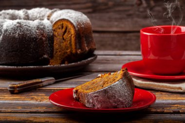 Koyu renk ahşap bir masada balkabaklı kek ve arka planda da bir fincan çay.