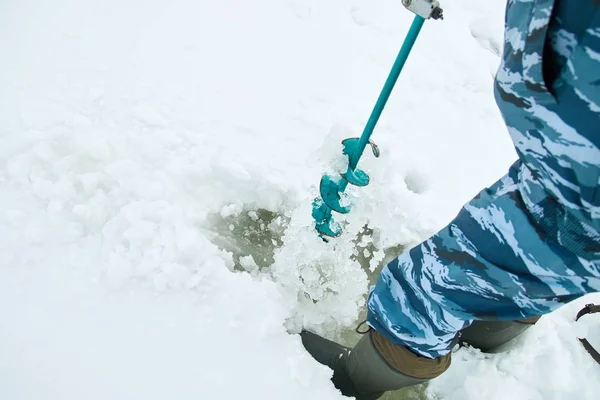 Winter fishing on ice. Man to drill a hole in the ice with an ice pick.