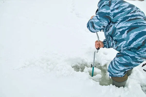 Winter fishing on ice. Man to drill a hole in the ice with an ice pick.