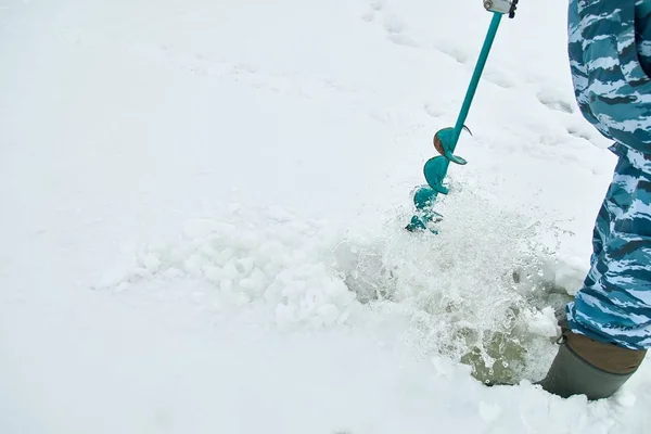 Winter fishing on ice. Man to drill a hole in the ice with an ice pick.
