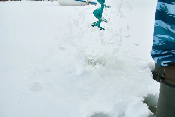 Winter fishing on ice. Man to drill a hole in the ice with an ice pick.