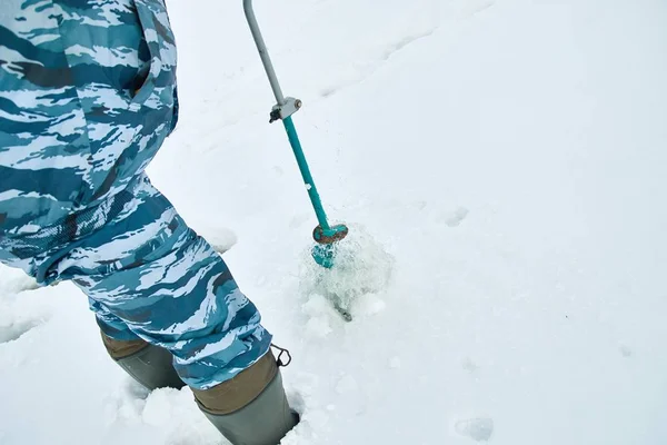 Winter fishing on ice. Man to drill a hole in the ice with an ice pick.