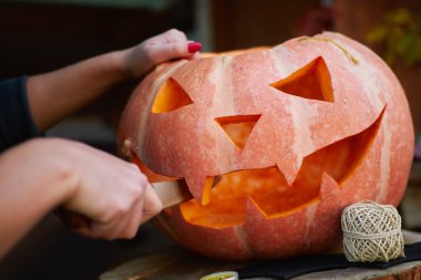 Kırmızı tırnaklı, balkabağına yüz kazıkan, açık tenli genç bir kız. Cadılar Bayramı ve Şükran Günü için geleneksel dekorasyon oluşturma