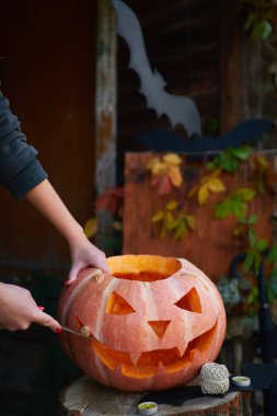 Kırmızı tırnaklı, balkabağına yüz kazıkan, açık tenli genç bir kız. Cadılar Bayramı ve Şükran Günü için geleneksel dekorasyon oluşturma