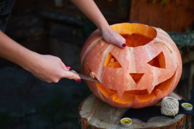 Kırmızı tırnaklı, balkabağına yüz kazıkan, açık tenli genç bir kız. Cadılar Bayramı ve Şükran Günü için geleneksel dekorasyon oluşturma