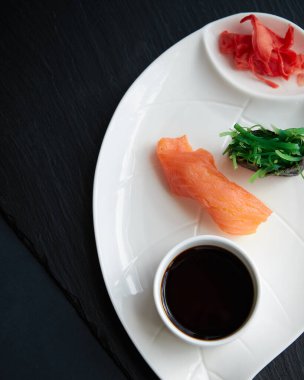 Soya soslu beyaz tabak, soya sosu, somon balıklı suşi, yeşil yosun ve koyu taştan bir arka planda kızıl kızıl kızıl.